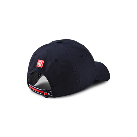 FootJoy fashion cap in navy blue, shown from the back. Features a red FootJoy logo on the adjustable strap with a striped red, white, and blue closure, adding a touch of sporty style. The design includes embroidered eyelets for breathability.