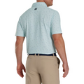 Model shown from the back, wearing the light mint green FootJoy Tweed Texture Polo. The back of the polo features the subtle tweed-like pattern with small, colorful specks, and the FootJoy logo is visible below the collar. The model is also wearing beige pants with a navy belt.