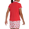 A woman facing away wears the FootJoy Floral Trim Short Sleeve Womens Polo in red, paired with a white skirt featuring a red floral pattern. Her hair is tied back, arms relaxed—creating a sporty yet stylish golf look by FootJoy.