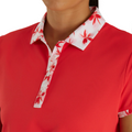 A person is seen from the neck down wearing the FootJoy Floral Trim Short Sleeve Womens Polo, a coral-colored golf shirt with a white collar and red floral-patterned placket by FootJoy, showcasing its stylish moisture-wicking design.