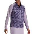 A person wearing a FootJoy Full-Zip Printed Pullover by FootJoy, featuring a lightweight design with a purple and white abstract pattern on the front and solid light purple sleeves, stands smiling.