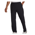 A man wearing FootJoy Men’s HydroLite X Rain Pants in black, paired with a white shirt and white shoes, stands with one hand by his side and the other on his hip.