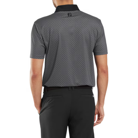 A man is shown from the back wearing a FootJoy Men's Checker Print Lisle Polo in Black/Grey with short sleeves, dark checker print, black collar, FJ logo on the back collar, and black pants. The polo is made from lightweight lisle fabric.