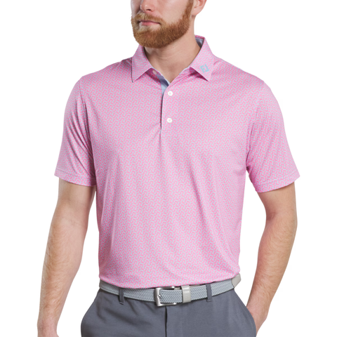 A man wears a FootJoy Men’s Citrus Print Lisle Polo in Lemonade/Skyway, gray pants, and a gray belt with a white buckle, standing with his hands relaxed at his sides.