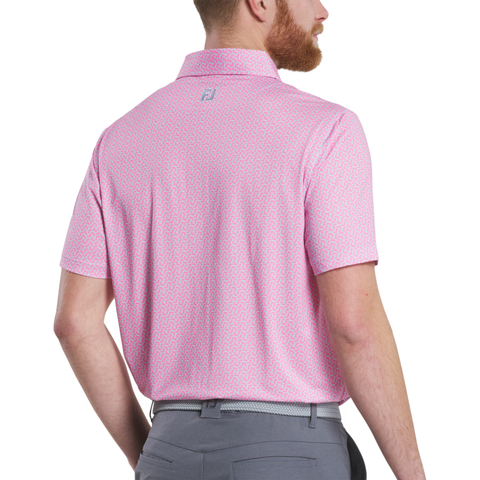 A man with a short beard, wearing a FootJoy Men’s Citrus Print Lisle Polo in Lemonade/Skyway, stands facing away. The light pink patterned golf shirt is tucked into gray pants and features a small FJ logo below the collar.