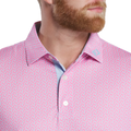 A man with a reddish beard wears the FootJoy Men’s Citrus Print Lisle Polo in Lemonade/Skyway—pink with blue and white patterns. Made from ProDry Performance Fabric, it features white buttons and a small logo on the collar. Only part of his face and torso show.
