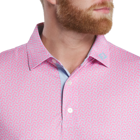 A man with a reddish beard wears the FootJoy Men’s Citrus Print Lisle Polo in Lemonade/Skyway—pink with blue and white patterns. Made from ProDry Performance Fabric, it features white buttons and a small logo on the collar. Only part of his face and torso show.