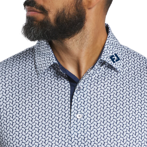 Close-up of a man with a beard wearing the FootJoy Men’s Citrus Print Lisle Polo in White/Navy, featuring a geometric pattern and blue "FJ" embroidery on the collar as he looks to the left.