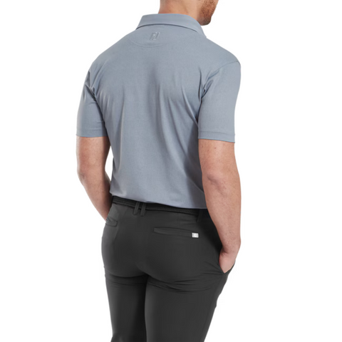 A man, seen from the back with hands in his pockets, wears black pants and a FootJoy Men's Etched Texture Print Lisle Polo in Flint. Part of his face is out of view.