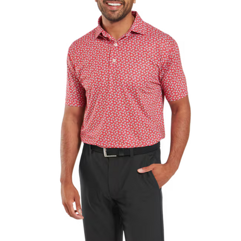 A man wearing a FootJoy Men's Floral Sketch Print Lisle Polo in Hibiscus/White with black pants stands with one hand in his pocket, smiling.