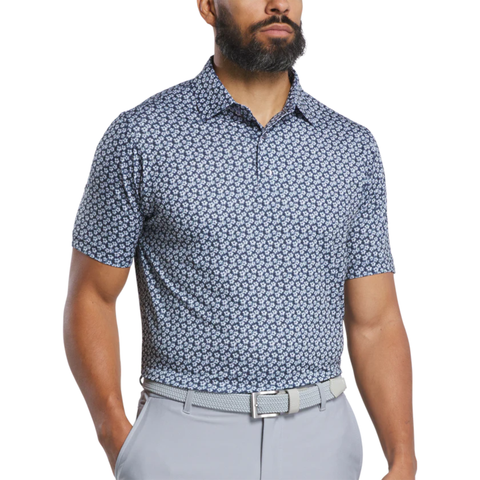 A bearded man stands with his hands by his sides, wearing a FootJoy Men's Floral Sketch Print Lisle Polo in navy/white, short sleeves and collar, tucked into light gray pants with a matching belt.