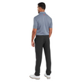 A man faces away from the camera wearing a blue FootJoy Men's Flower Bud Foulard Lisle Polo in Flint, featuring moisture-wicking fabric, paired with black pants and white shoes, on a plain white background.