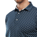 A close-up of a man wearing the FootJoy Men's Flower Bud Foulard Lisle Polo in navy, showcasing its white and yellow floral print and ProDry performance fabric. The image is cropped at his mouth and mid-torso to highlight the shirt’s subtle design.