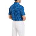 A man wearing a FootJoy Men's Golf Course Doodle Polo with a white abstract pattern and white pants stands facing away from the camera, arms slightly crossed.