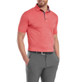 A man in a FootJoy Men's Heather Lisle Polo in Hibiscus, gray pants, and a black belt stands with hands in his pockets against a white background.