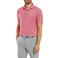 A man smiles with one hand in his pocket, wearing the FootJoy Mens Lisle Houndstooth Geo Print Polo in Hibiscus, tucked into light gray pants with a brown belt.