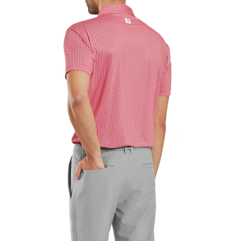 A man, seen from behind, wears a FootJoy Men's Lisle Houndstooth Geo Print Polo in Hibiscus and light gray pants, his left hand in his pocket.