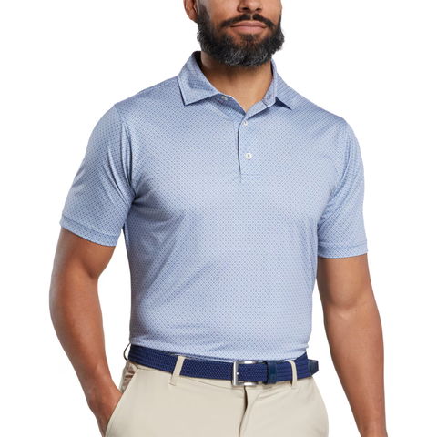 A man wearing a FootJoy Men's Loop Print Lisle Polo in White/Skyway, paired with beige pants and a navy blue belt, stands with his arms relaxed at his sides against a white background.