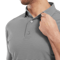 A man wearing the FootJoy Mens Micro Feeder Stripe Lisle Polo in black/grey adjusts the collar with his right hand, showing only the lower half of his face and upper torso.