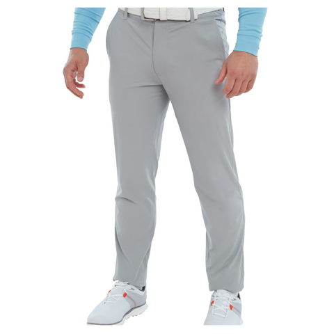 A person wearing FootJoy Mens Par Trousers in light gray, paired with a white belt, white shoes, and a light blue long-sleeve shirt stands against a white background. The moisture-wicking fabric from FootJoy ensures all-day comfort.