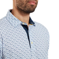 A man, shown from the chest up with a trimmed beard, wears the FootJoy Mens Pique Solid Figure Print Lisle Polo in White/Navy, featuring a blue geometric pattern and navy inner collar. This moisture-wicking shirt keeps you cool and comfortable.