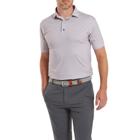 A man wears a light purple FootJoy Men's Scallop Shell Foulard Lisle Polo, dark gray pants, and a black-and-white woven belt with brown accents. The moisture-wicking lisle polo by FootJoy keeps him comfortable and stylish.