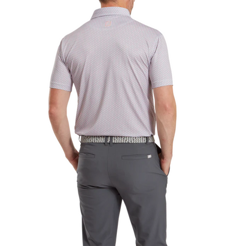 A man stands with his back to the camera, wearing a FootJoy Men's Scallop Shell Foulard Lisle Polo, dark gray pants, and a patterned belt. His hands are in his pockets against a plain white background.