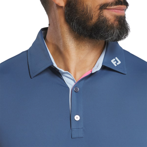 A man with a trimmed beard models the FootJoy Men's Solid Pique with Trim Polo in Dark Denim/Skyway, featuring an embroidered white logo on the collar. Only his lower face and upper torso are visible, highlighting this stylish golf shirt.