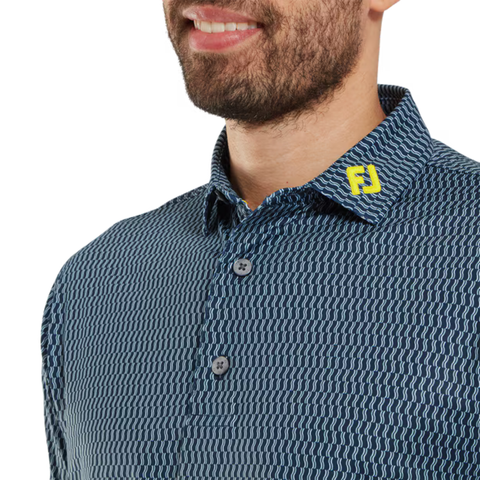 A bearded man wears a FootJoy Men’s Wiggle Print Lisle Polo in navy/white. The button-down features a ProDry Performance Fabric collar with yellow FJ initials. Only his lower face and upper torso are shown.