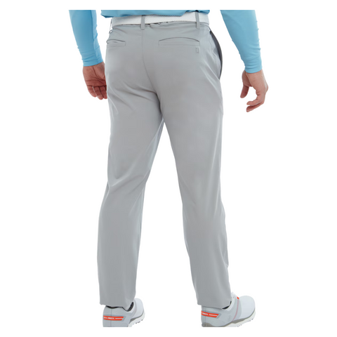 A person wearing FootJoy Mens Par Trousers in light gray, a light blue shirt, and white shoes with orange accents, shown from the back against a white background.