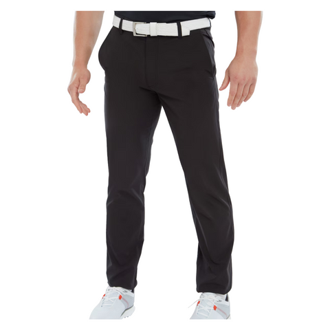 A person stands with arms relaxed at their sides, wearing black FootJoy Mens Par Trousers by FootJoy, a white belt, and white sneakers. The upper body is partially visible against a plain white background.