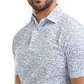 A man wearing the FootJoy Scottish Town Mens Print Polo—by FootJoy—a light blue, short-sleeve golf shirt featuring a geometric pattern of small houses; only his torso and lower face are visible.