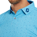Close-up of a person wearing the FootJoy Tweed Texture Mens Polo by FootJoy—a light blue, speckled four-way stretch golf shirt with a buttoned collar and embroidered dark blue FJ logo; the persons face is mostly out of frame.