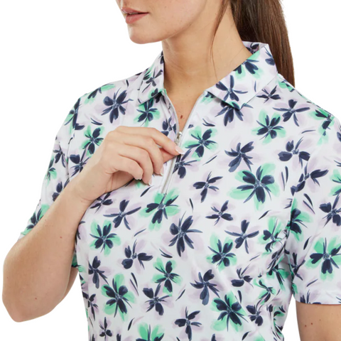 A woman wears a FootJoy Women's 1/4 Zip Short Sleeve Floral Shirt in Lavender/Mint/Teal, partially unzipping the front; only the lower part of her face and upper body are visible.