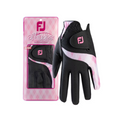 A black and pink FootJoy Women’s Attitudes Glove is shown beside its packaging, which displays the same glove behind a clear window with the FootJoy logo and Attitudes in a stylized font.