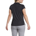 A woman is shown from the back wearing a FootJoy Women's Cap Sleeve Print Shirt in Black Animal Print, paired with light gray pants against a white background. This stylish moisture-wicking golf shirt combines comfort and performance.