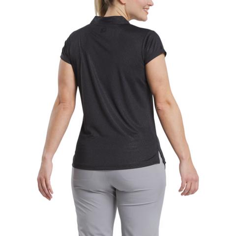 A woman is shown from the back wearing a FootJoy Women's Cap Sleeve Print Shirt in Black Animal Print, paired with light gray pants against a white background. This stylish moisture-wicking golf shirt combines comfort and performance.