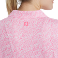 A person with blonde hair in a ponytail wears the FootJoy Women’s Cap Sleeve Print Shirt in Pink Lemonade, featuring a pink and white dotted pattern, stretch fabric, and a small pink logo on the back below the collar.