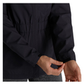 A person adjusts the cuff of a dark waterproof FootJoy Women’s HydroLite Jacket with a hook-and-loop fastener. The jacket features an elastic waistband, and the wearer is dressed in gray pants.