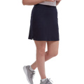 A woman shown from mid-torso down stands with one leg slightly bent, wearing a FootJoy Womens Interlock Stretch Skort in navy, light gray sneakers, and a white top.