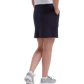 A person wearing a FootJoy Womens Interlock Stretch Skort in navy, a white shirt, and gray athletic shoes stands with hands in skort pockets, photographed from behind against a white background.