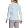 A woman with blonde hair in a ponytail is shown from the back, wearing FootJoy Women’s Long Sleeve Sun Protection Shirt in Skyway/Navy and gray pants against a white background.