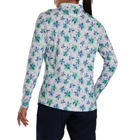 A person stands facing away, wearing the FootJoy Women's Long Sleeved Floral Shirt with a blue and green floral pattern, paired with dark pants. Their hair is tied back, highlighting the shirt's collared design and the FootJoy brand style.