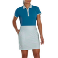 A woman stands against a white background, wearing a short-sleeve blue polo with a plaid collar and the FootJoy Women's Performance Knit Skort, which offers moisture-wicking comfort.