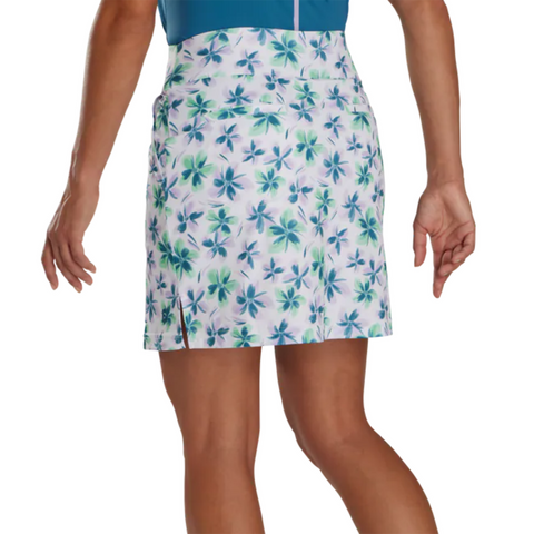 A person in a blue top and a FootJoy Women's Performance Knit Skort with a blue and green floral print is shown from the back. The FootJoy skort has moisture-wicking fabric, a side slit, and the person's arms rest at their sides.