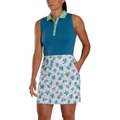A woman wearing a sleeveless teal polo top and a FootJoy Women's Performance Knit Skort by FootJoy with a blue and green floral pattern, featuring moisture-wicking fabric for comfort, stands with one hand in her pocket.