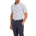 A model wearing the FootJoy Golf Course Doodle Polo, showcasing its white background with a playful navy and red doodle pattern. The shirt is paired with dark navy pants and a blue belt.