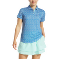 A person wearing a FootJoy Womens Floral Print Short Sleeve Shirt and a light blue tiered skirt stands with one hand in their pocket, smiling.