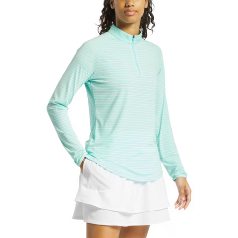 A woman wears the FootJoy Womens 1/4 Zip Long Sleeve Sun Protection Shirt in light blue, paired with white layered athletic shorts, standing with one hand in her pocket.