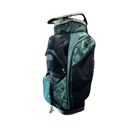 The Ogio 2026 Silencer Cart Bag | Paradise, in black and green with a tropical leaf pattern and club-locking technology, features multiple zippered pockets and a top handle, shown against a white background.